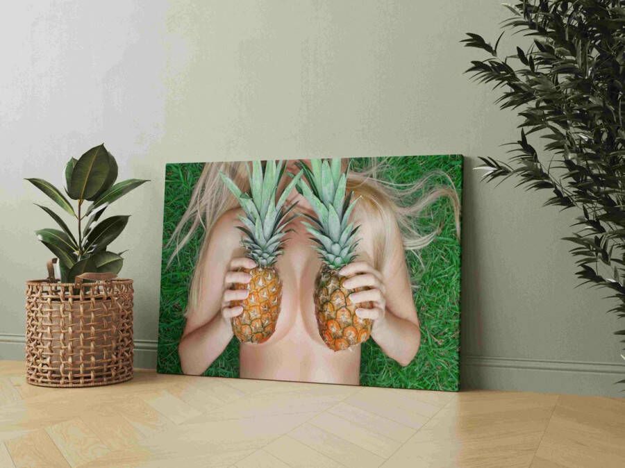 Een jonge vrouw houdt ananassen bij haar borst terwijl ze op het gras ligt. BH van ananas. Tropische bescheidenheid. Schilderijen 1199948278 60x80cm